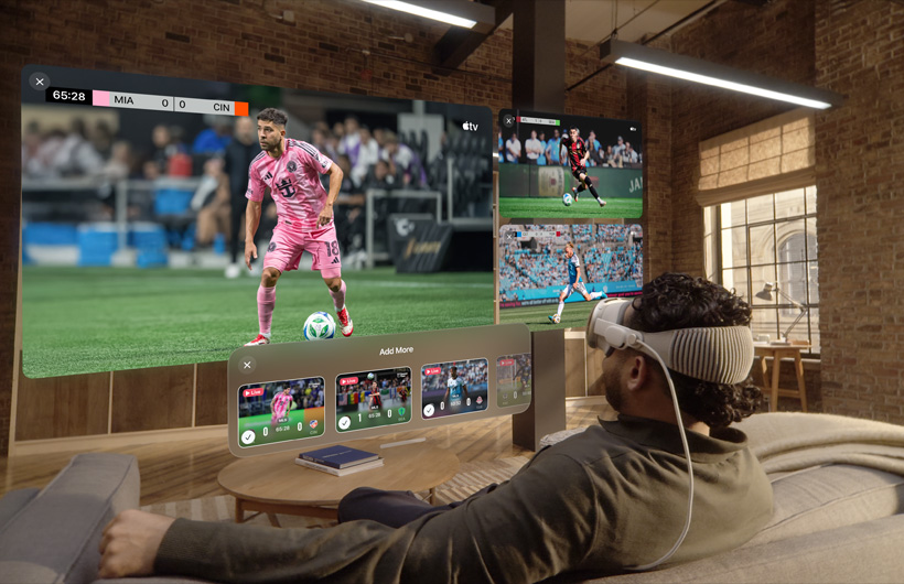 Person wearing Apple Vision Pro is sitting on a couch in a living room, displayed in front of them is a large video screen alongside two smaller screens, each showing a different sporting event. Below the large screen is a selection window that reads: Add More