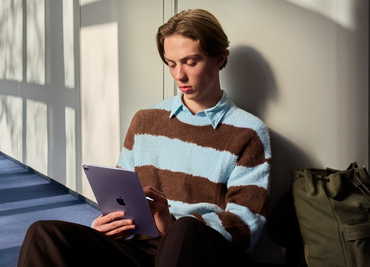 En person som sitter på golvet i ett ljust rum och använder iPad och Apple Pencil.