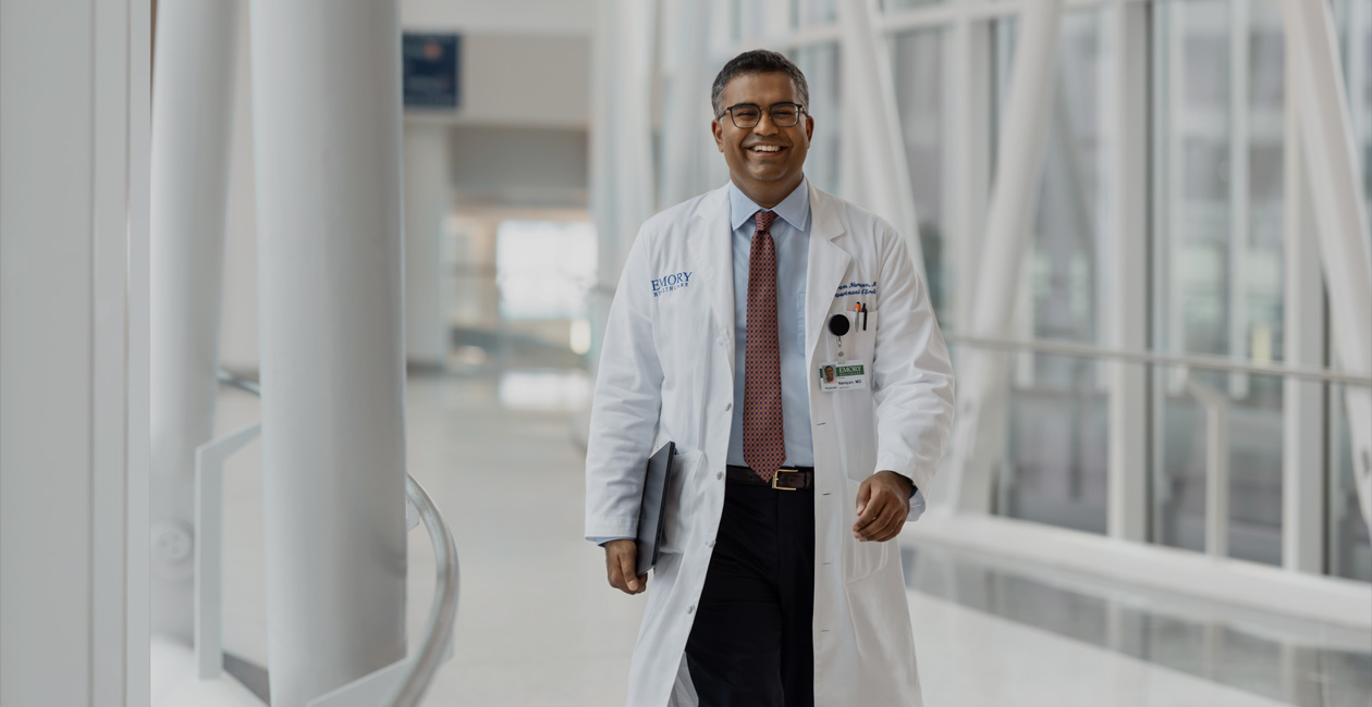 A doctor holding a MacBook under their right arm while walking.