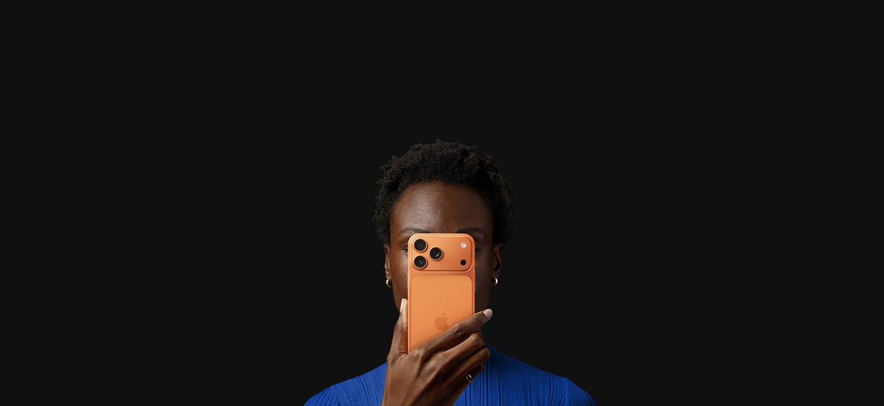 Una persona tiene iPhone 17 Pro davanti al viso, con la parte posteriore rivolta in avanti, colore arancione cosmico