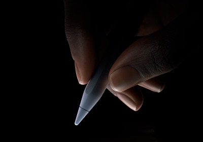 Mão a segurar a parte inferior do Apple Pencil Pro entre o polegar e o indicador, em posição de escrita.