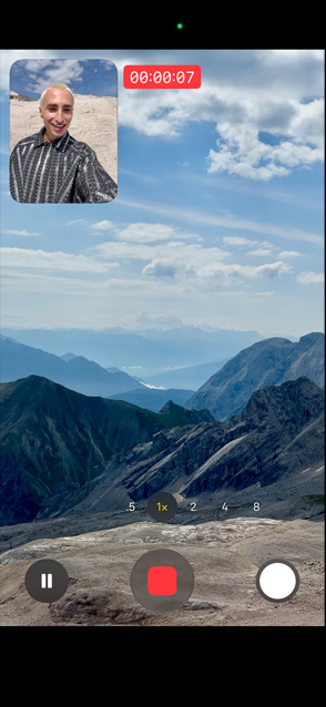 En person demonstrerer video med dobbelt optagelse ved at optage sig selv med kameraet på forsiden og samtidig optage de naturskønne bjerge med kameraet på bagsiden