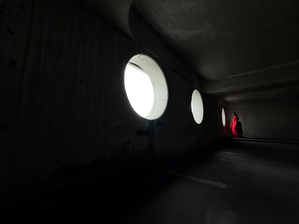 En kvinde i en rød kjole står i et tomt rum og bliver fotograferet. Fotos-appen skifter mellem brændvidder for at demonstrere mulighederne i Pro-kamerasystemet og viser: 13 mm