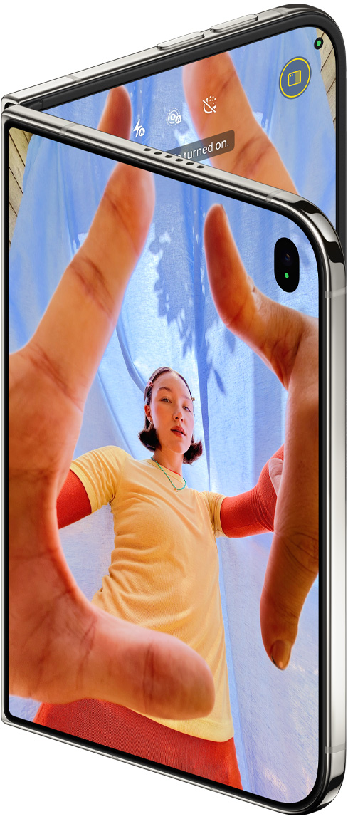 iPhone Duo, Star White color, slightly open, Camera app on outer display with Center Stage front camera, inner display shows Photos app library