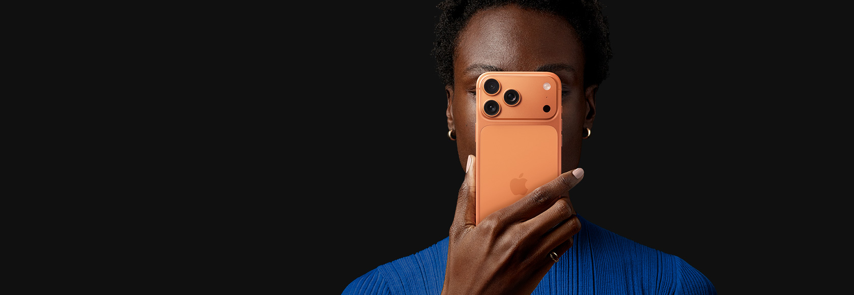 Een persoon houdt iPhone 17 Pro voor het gezicht, met de achterkant naar buiten gericht, kleur Kosmisch Oranje