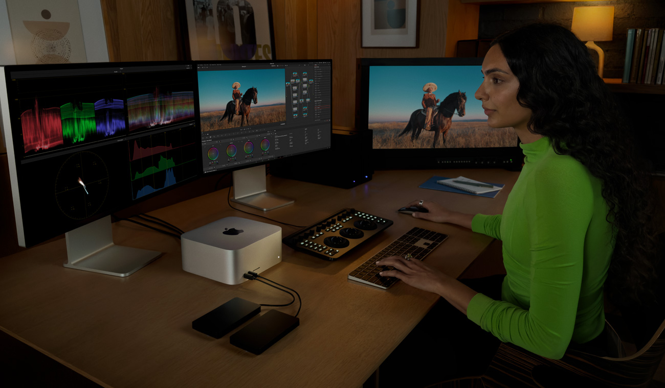 Uma profissional usando o Mac Studio com três monitores para editar arquivos.