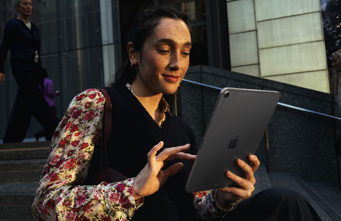 Una persona sentada en las escaleras afuera de un gran edificio usa un iPad Air de 11 pulgadas gris espacial, con una conexión Wi-Fi que se mantiene estable mientras alterna entre diferentes redes