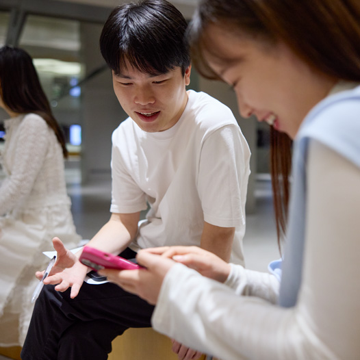 Two people talk as they look down at an iPhone that one of them holds and navigates