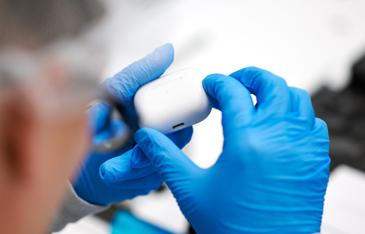 Two hands wearing latex gloves hold up an AirPods case